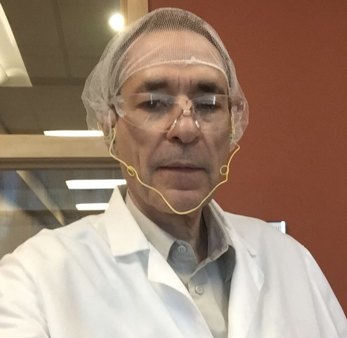 Man in lab coat and hairnet indoors.
